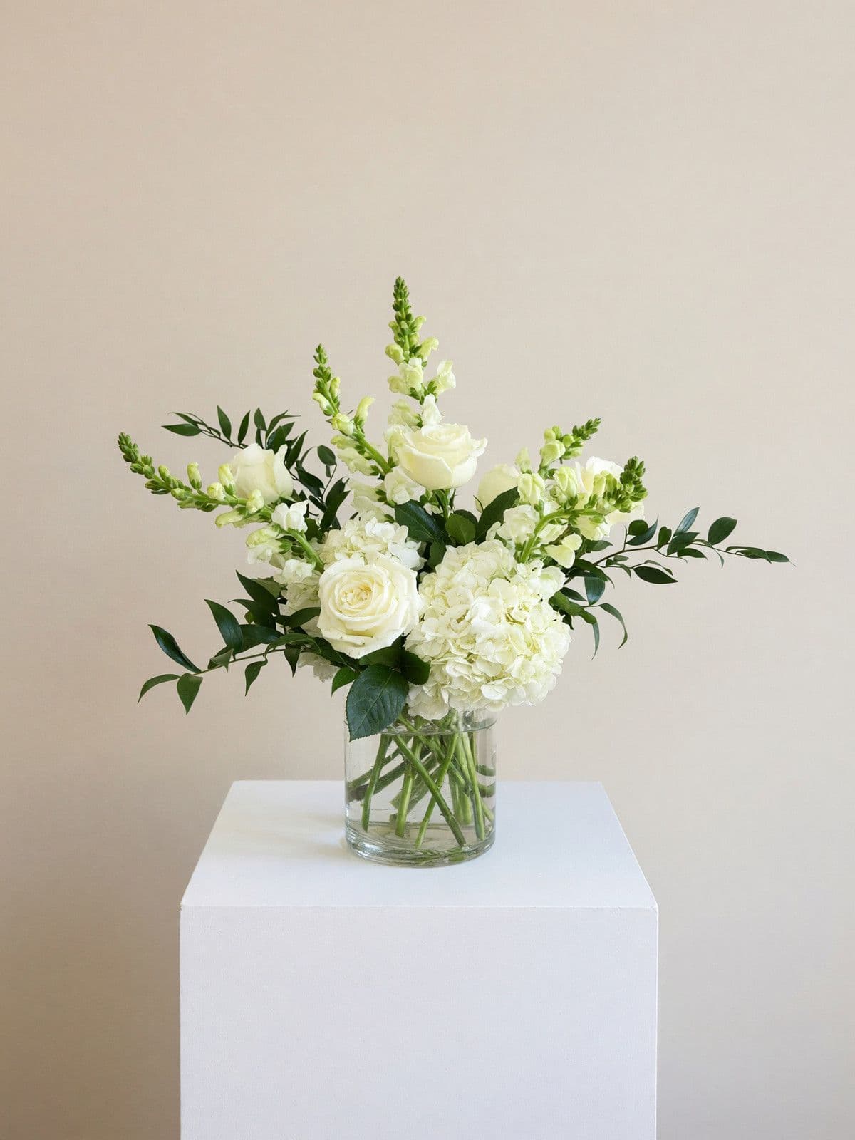 White roses, snapdragons and hydrangea in a clear glass vase.